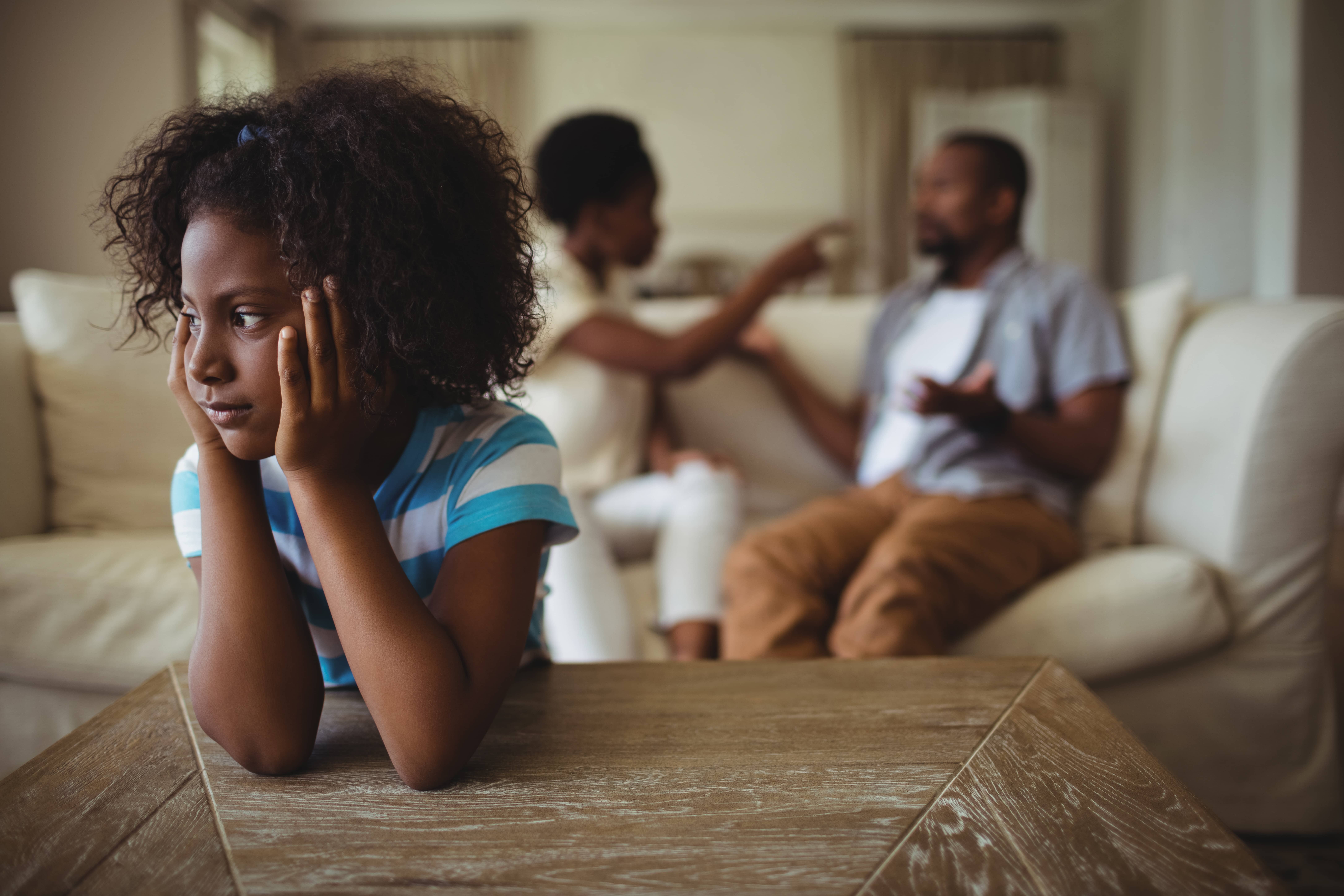 Sad black girl listening to her parents argue.