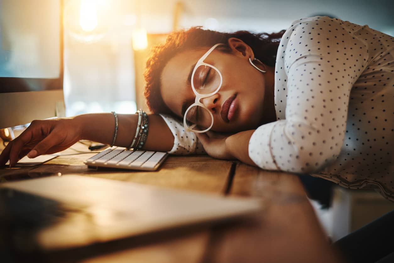 A woman with head down on her desk exhausted from fighting procrastination.