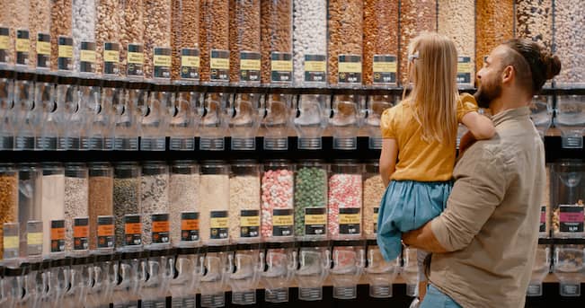 Father and daughter choosing snacks at a grocery supermarket facing dozens of bins.