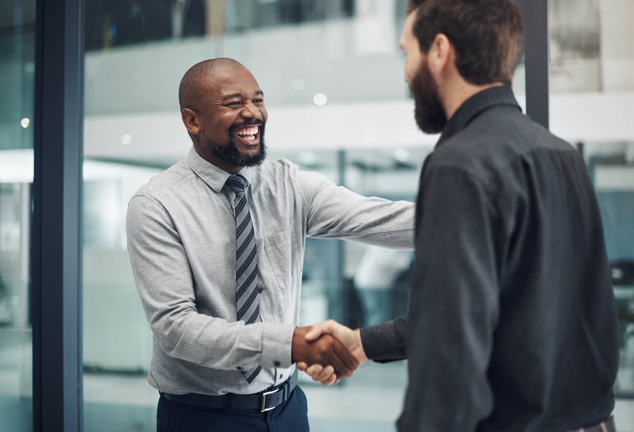 A mature businessman with a smile shaking hands with a new hire in a modern office.