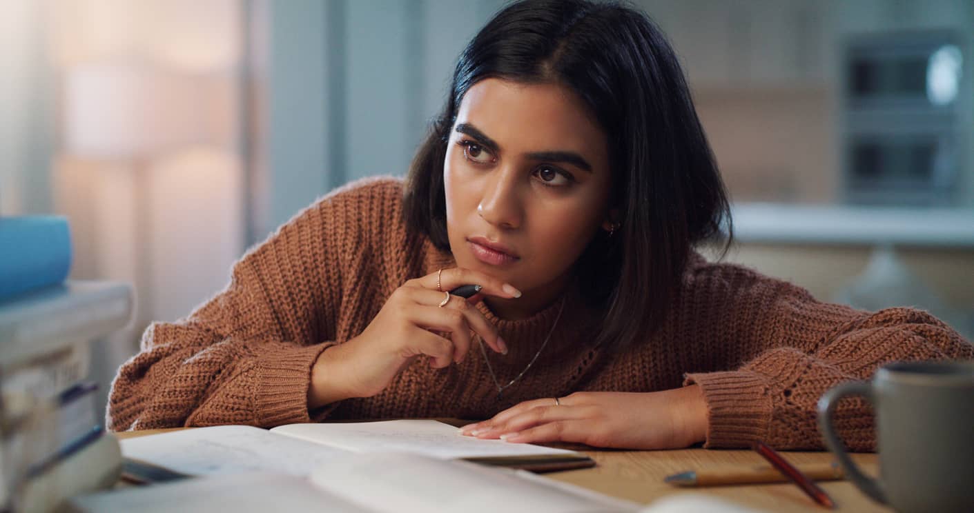 A young woman with a pensive expression practicing emotional regulation by journaling.