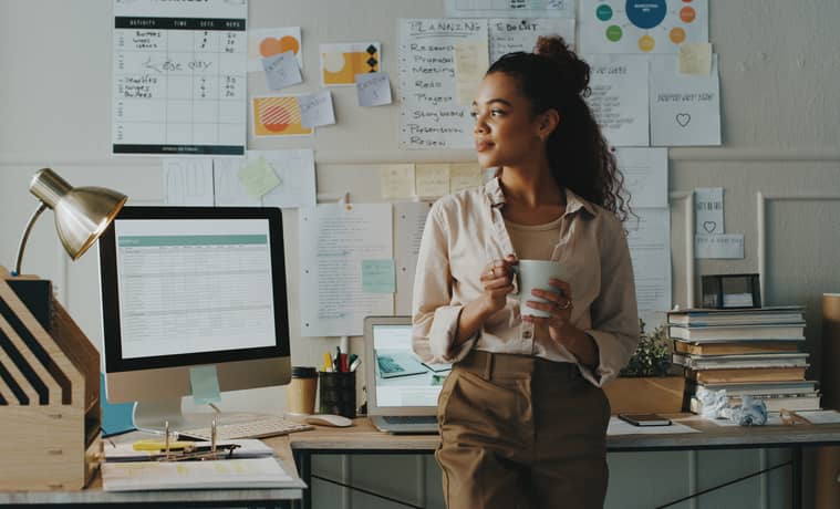 An attractive young businesswoman contemplative recent events while holding a cup of coffee in her home office.