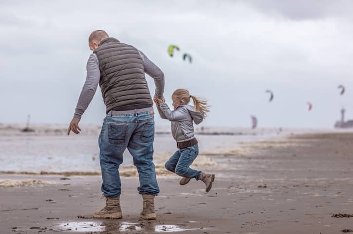 A father and his daughter playing family games on a beach.