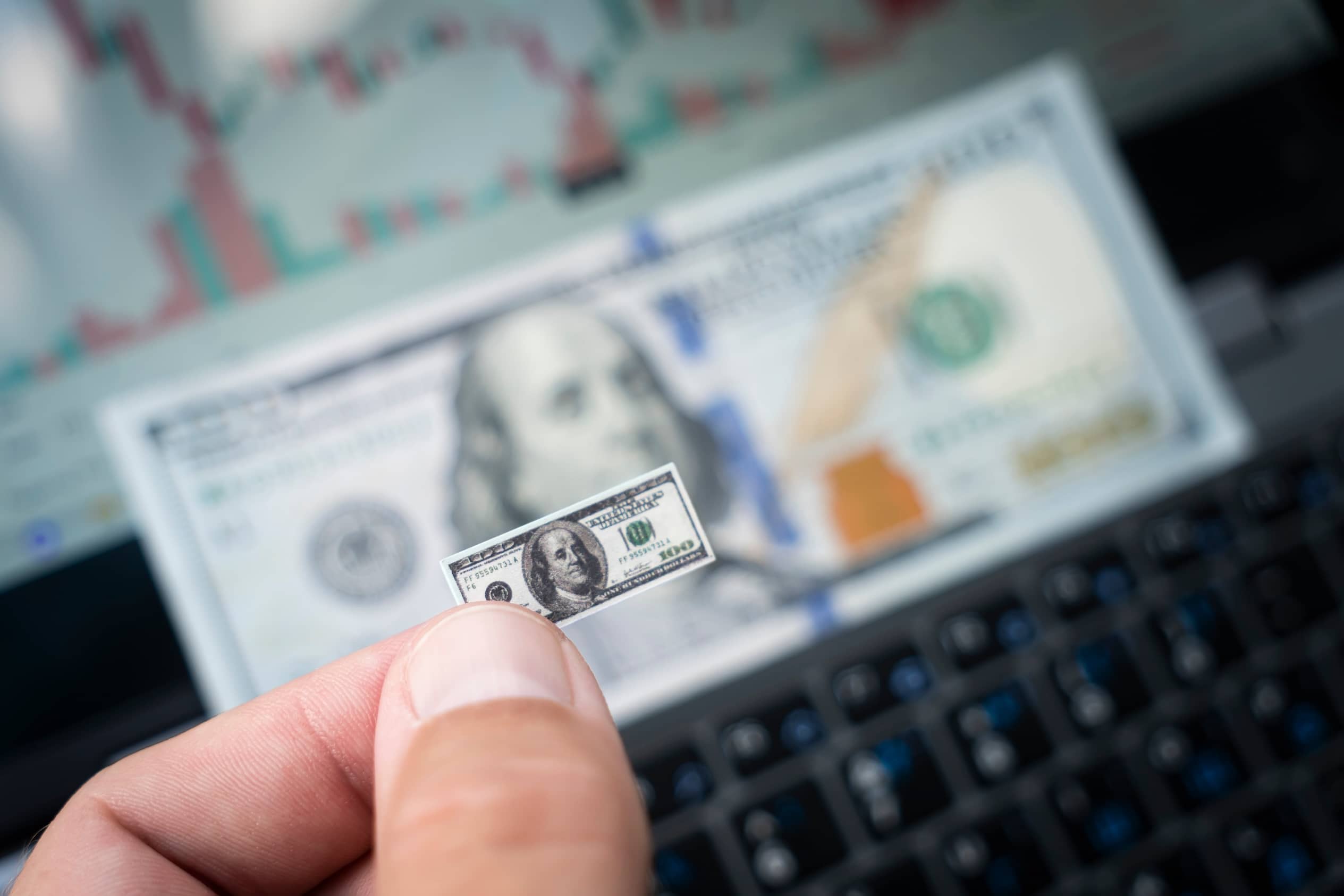 A tiny hundred dollar bill against the background of real-life sized money.