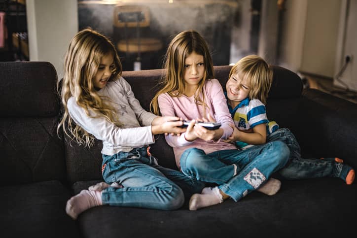 Small siblings fighting over a remote control in the living room.