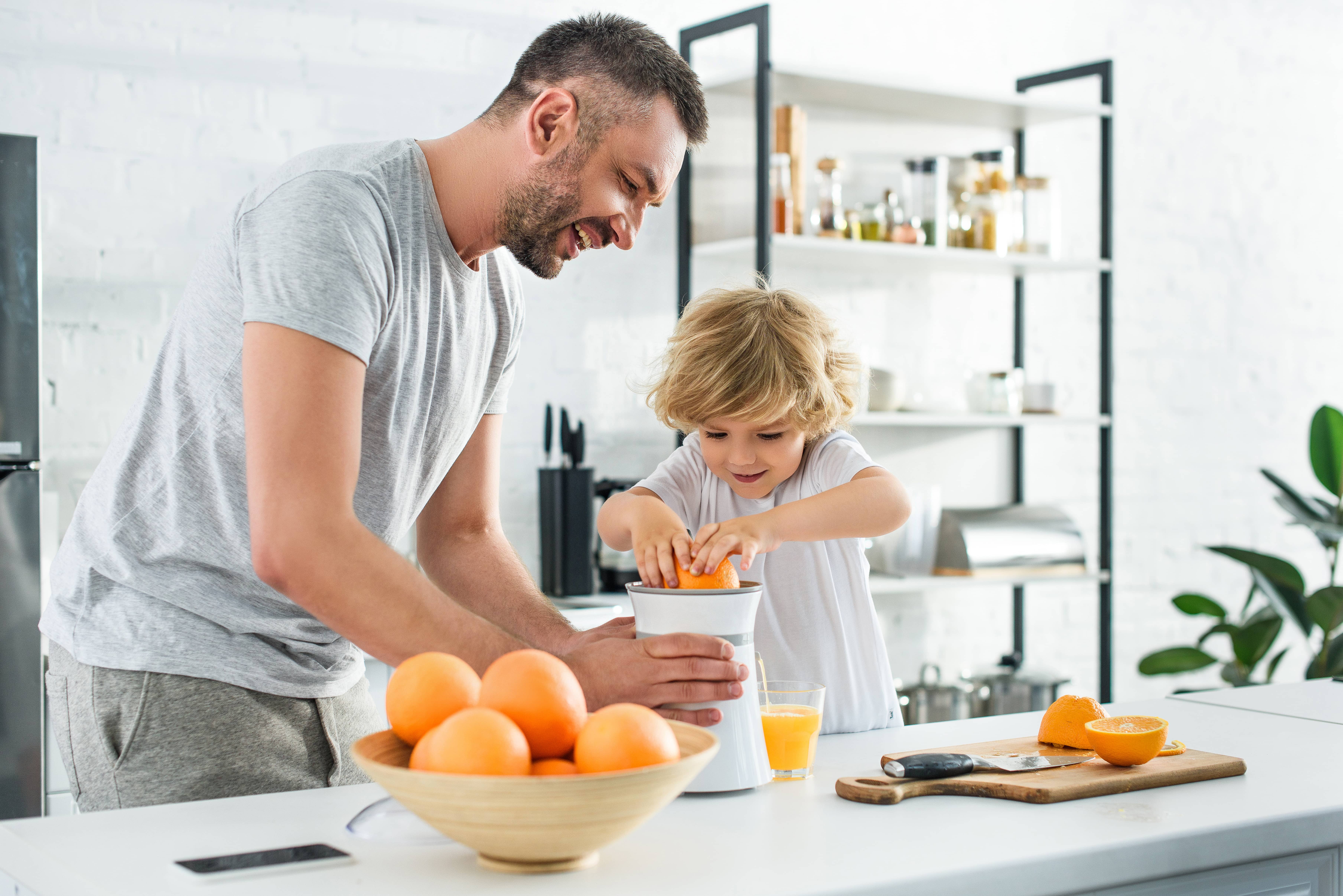 Smiling father and his preschool son juicing oranges in the kitchen.