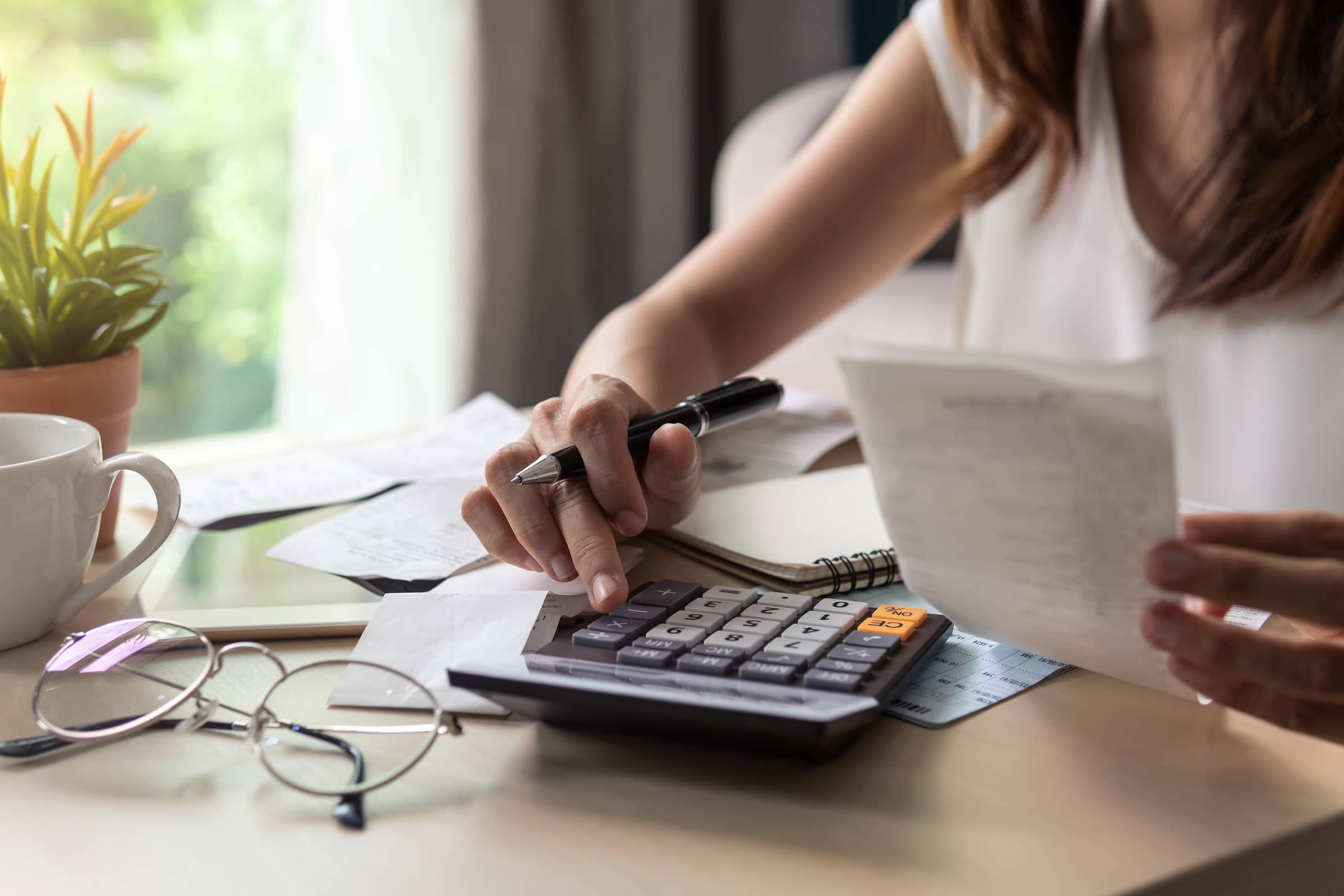 Stressed young woman calculating expenses, checking bills, and bank account balances at a desk.