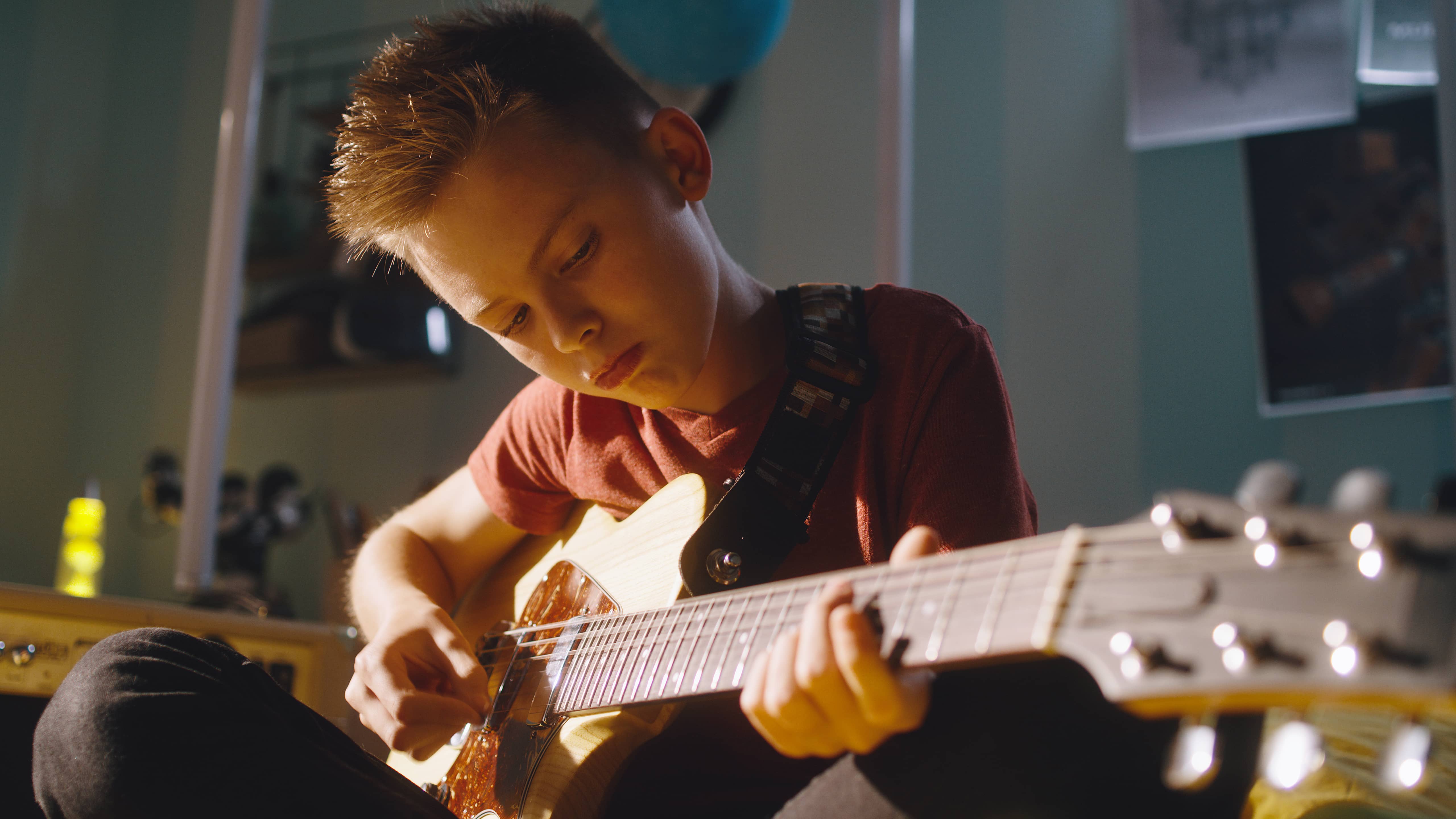 Teen boy playing guitar in his bedroom to destress and self-regulate himself.