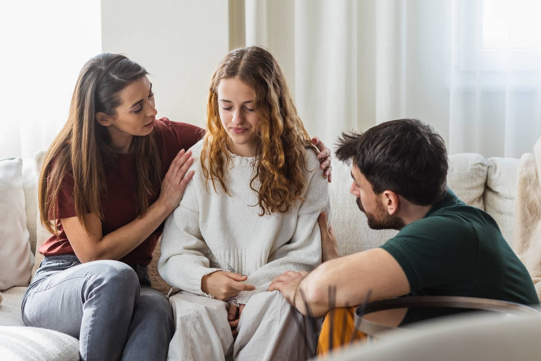 Teenage girl feeling down while her parents empathize and comfort her.