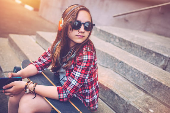 Teenage girl with a skateboard listening to music
