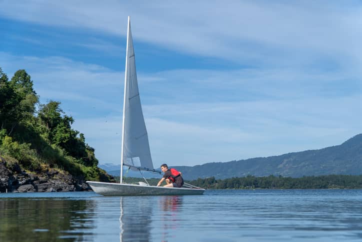 Teenager sailing on a beautiful summer day on the lake with a small sailboat.