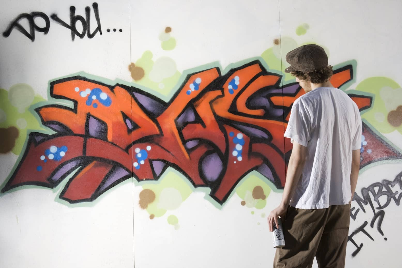 A teenager rebelling by painting graffiti with artist spray on building wall.