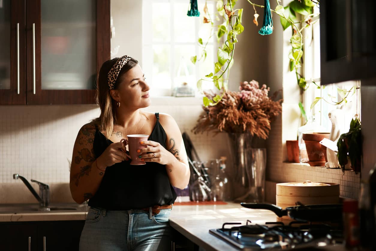 A young woman reflecting on her values as she looks out the kitchen window and sips coffee.