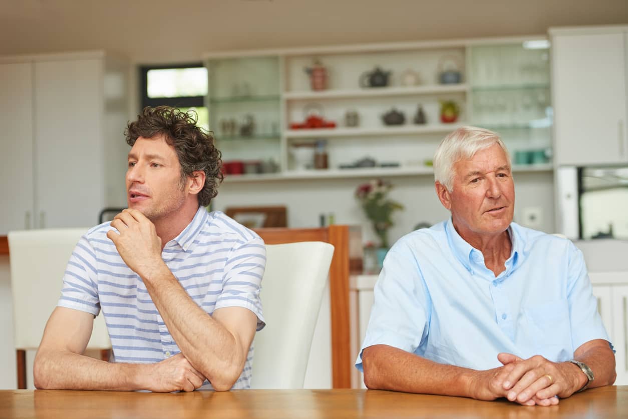Adult son sitting while disconnected from his father; both looking away and not talking to each other.