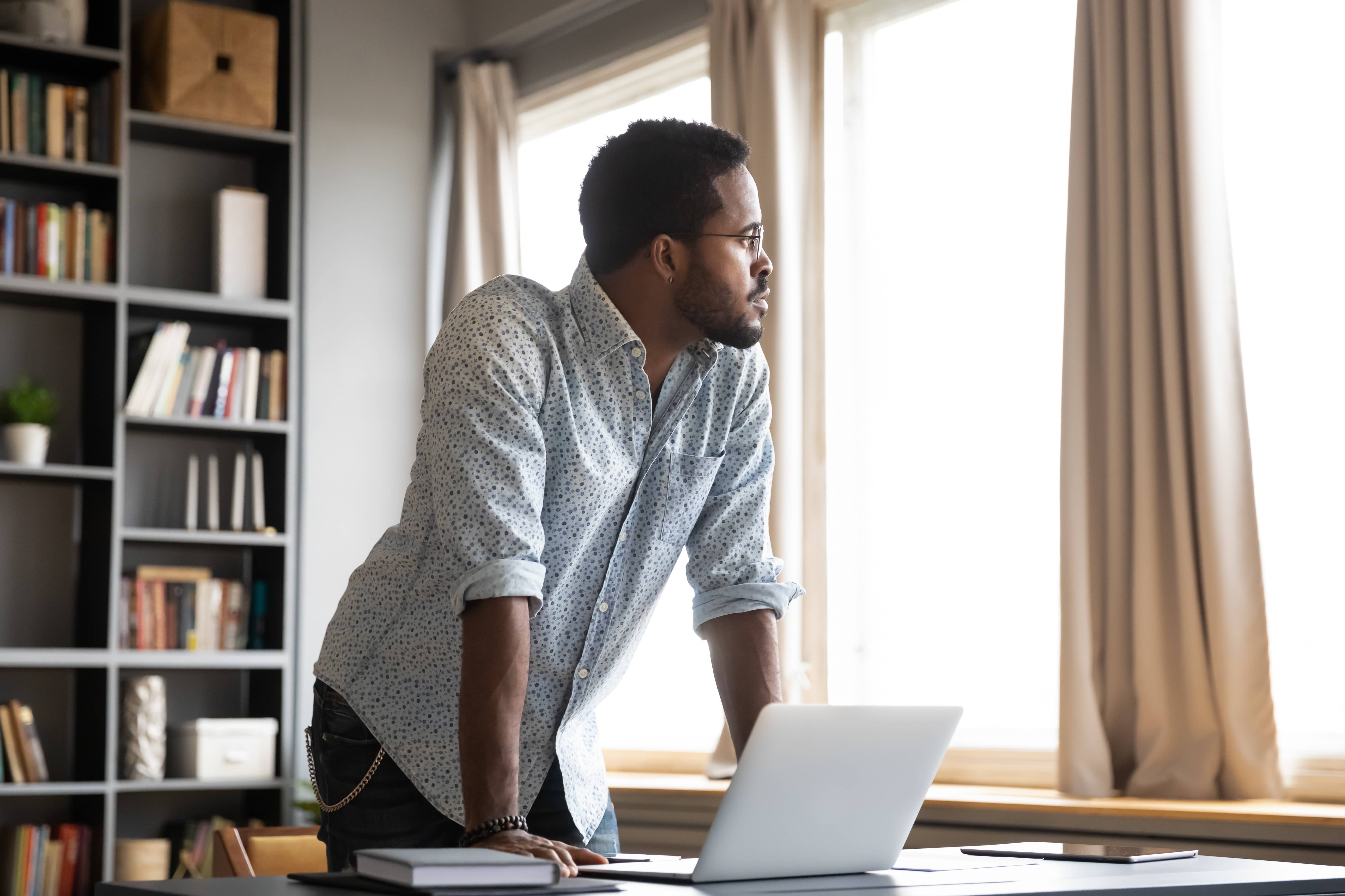 Thoughtful African American businessman leaning on his desk and looking away.