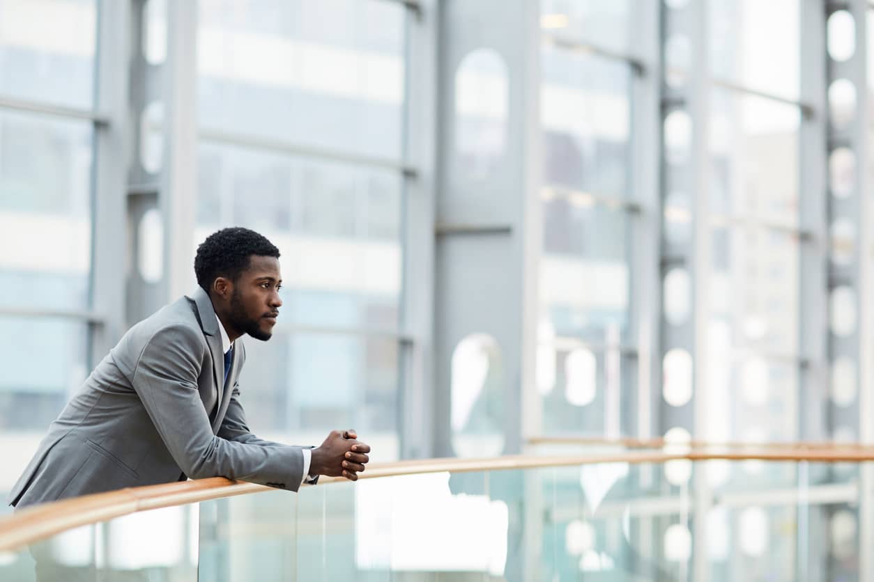 Thoughtful businessman leaning on a railing with hands cuffed.