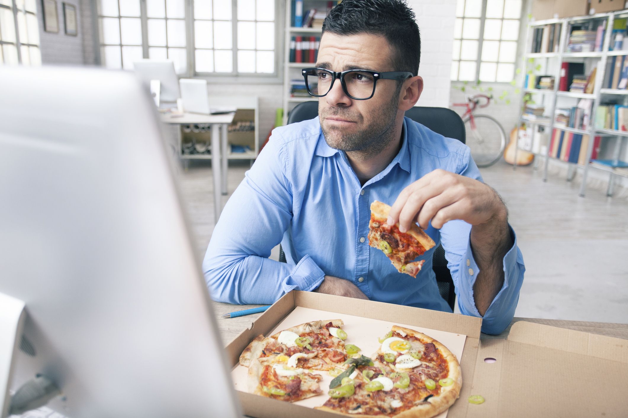 Tired businessman eating pizza at the office avoiding his anxiety