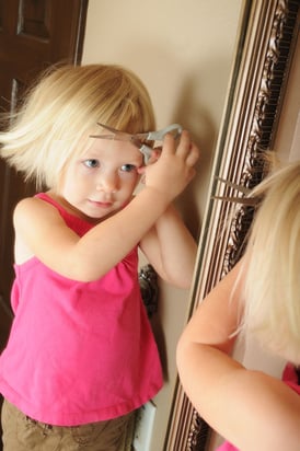 Preschool girl cutting her hair; much of children's behavior is innocent exploration