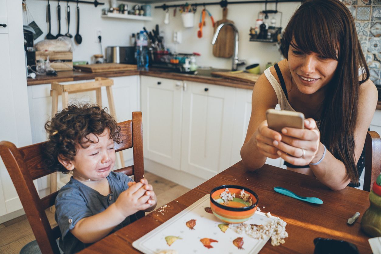 A mom ignoring her crying toddler while she scrolls her social media feed.