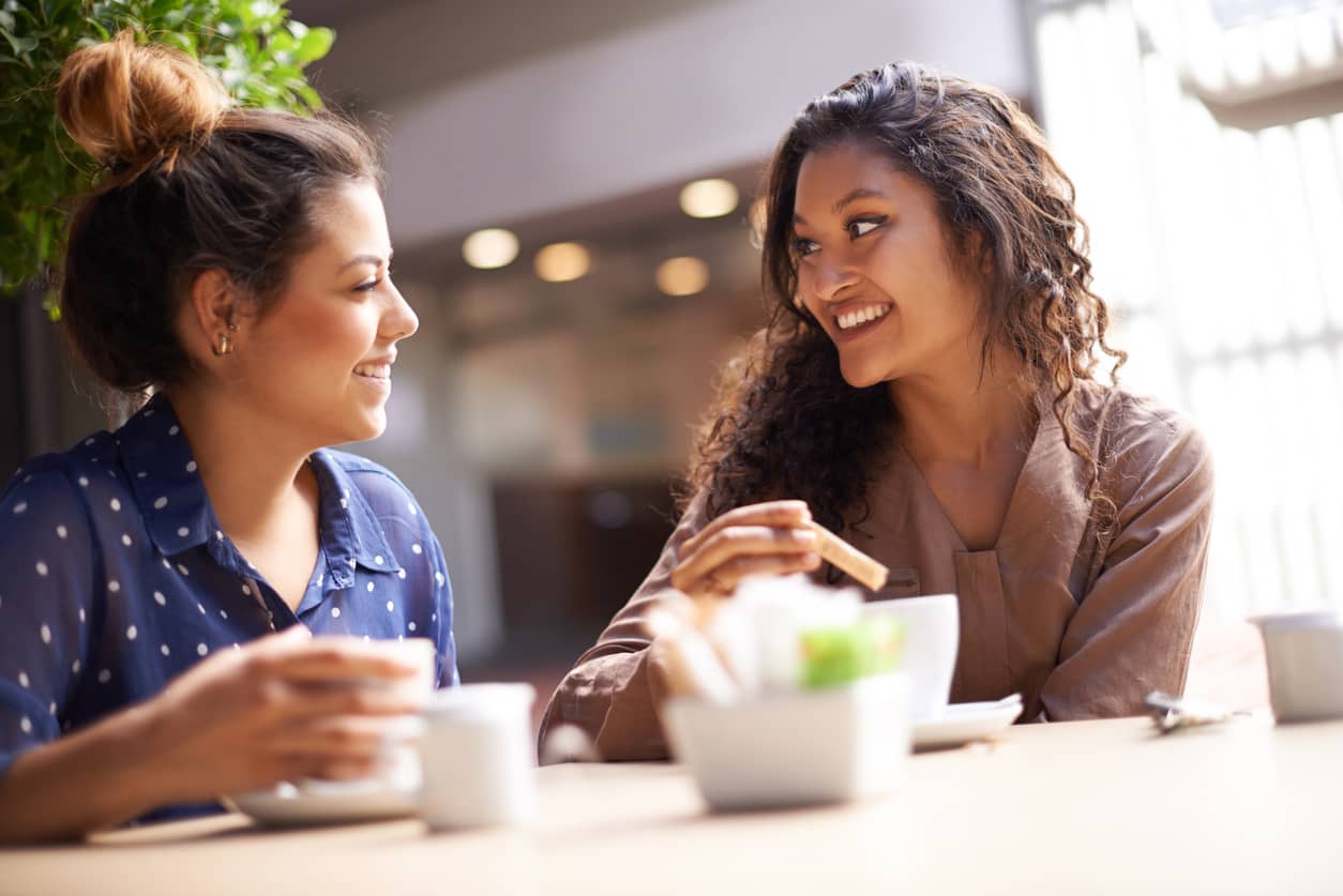 Two smiling women catching up over coffee.