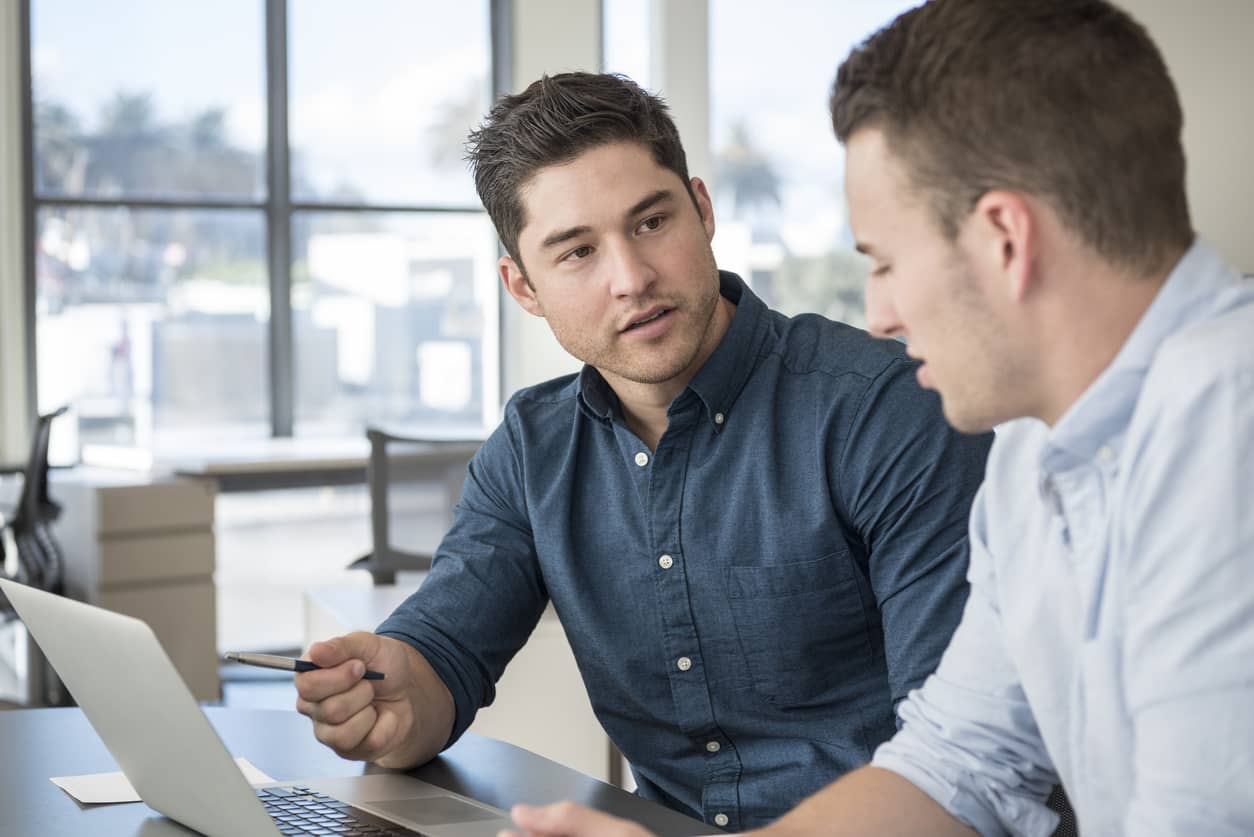 Two young businessmen in a meeting using a laptop and discussing a project with social intelligence..