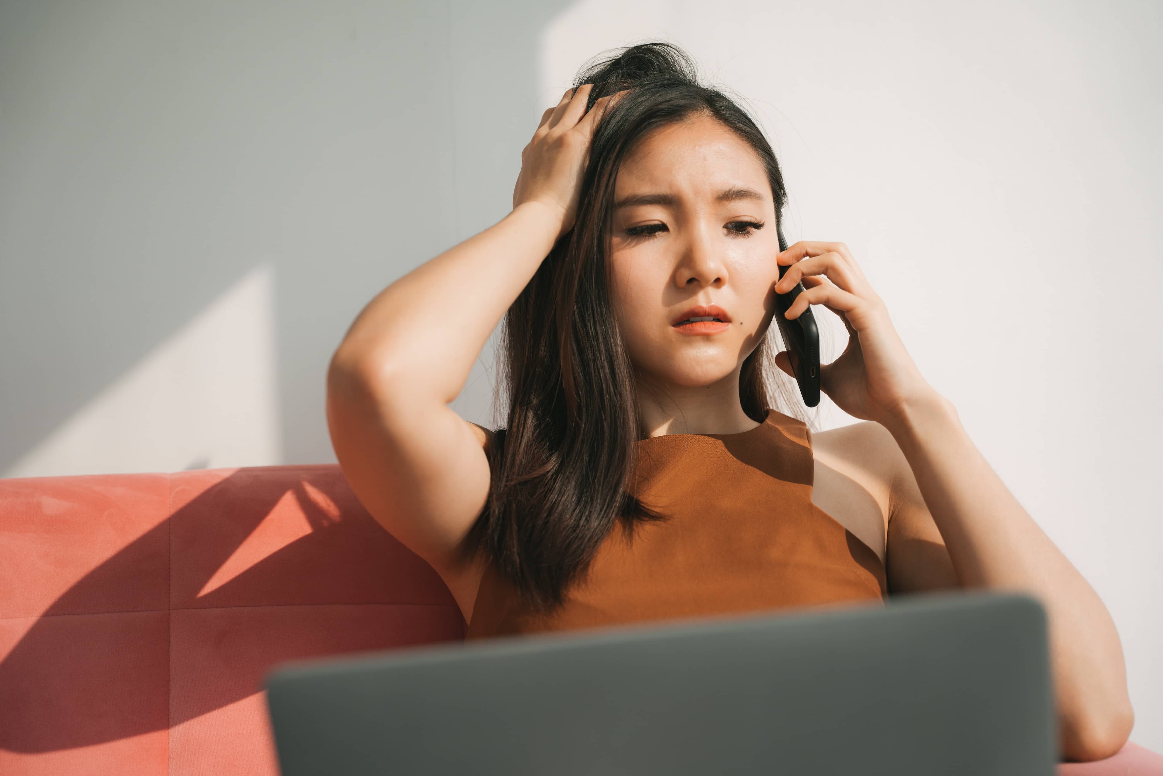 A super stressed Asian businesswoman working on laptop and talking on her smartphone.