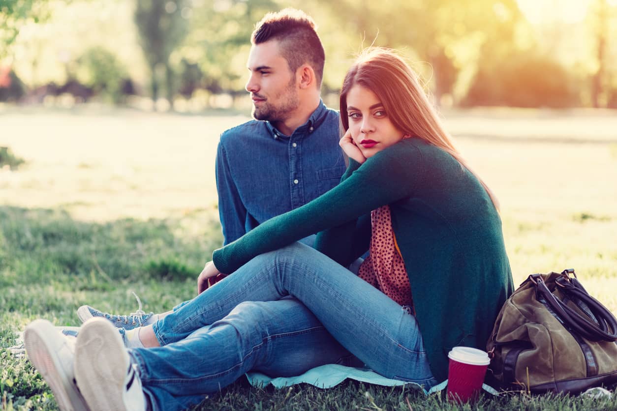 Unhappy young couple sitting on the grass in a city park.