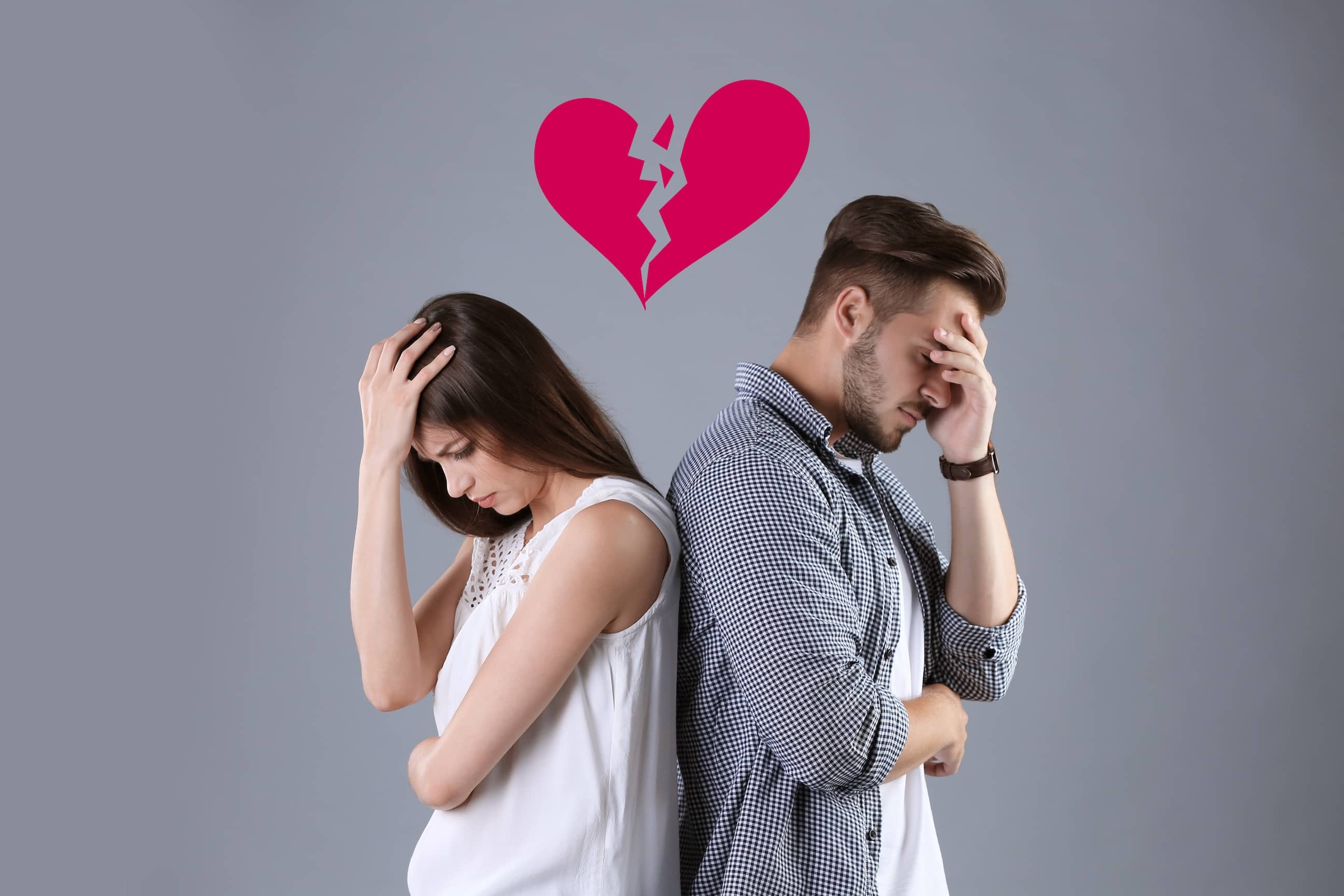An upset young couple with their backs to each other with broken heart on grey background representing the empathy gap in a relationship.