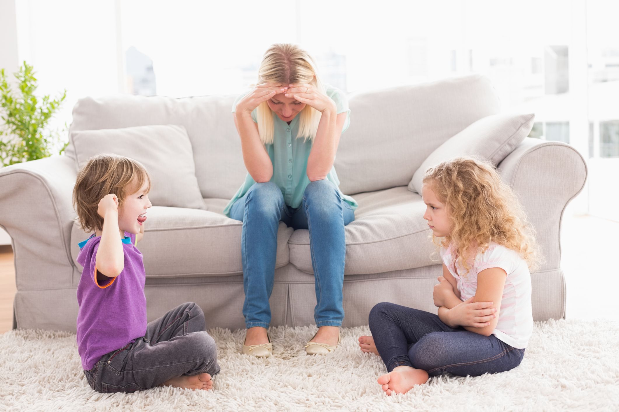 Upset mother sitting on sofa while brother teasing his sister