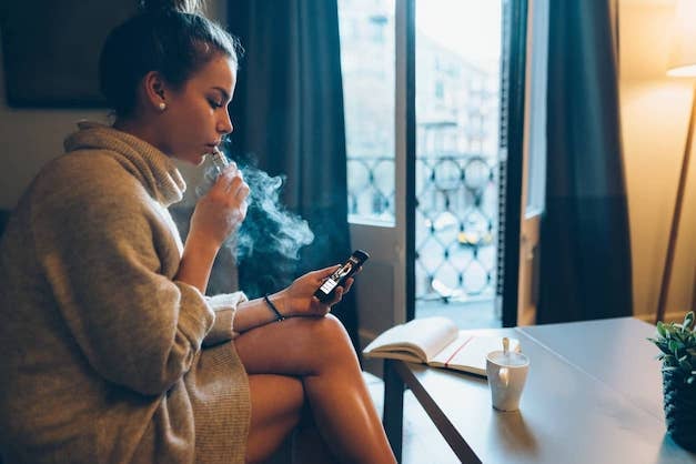 Young teen girl surfing social media on her smartphone while vaping.
