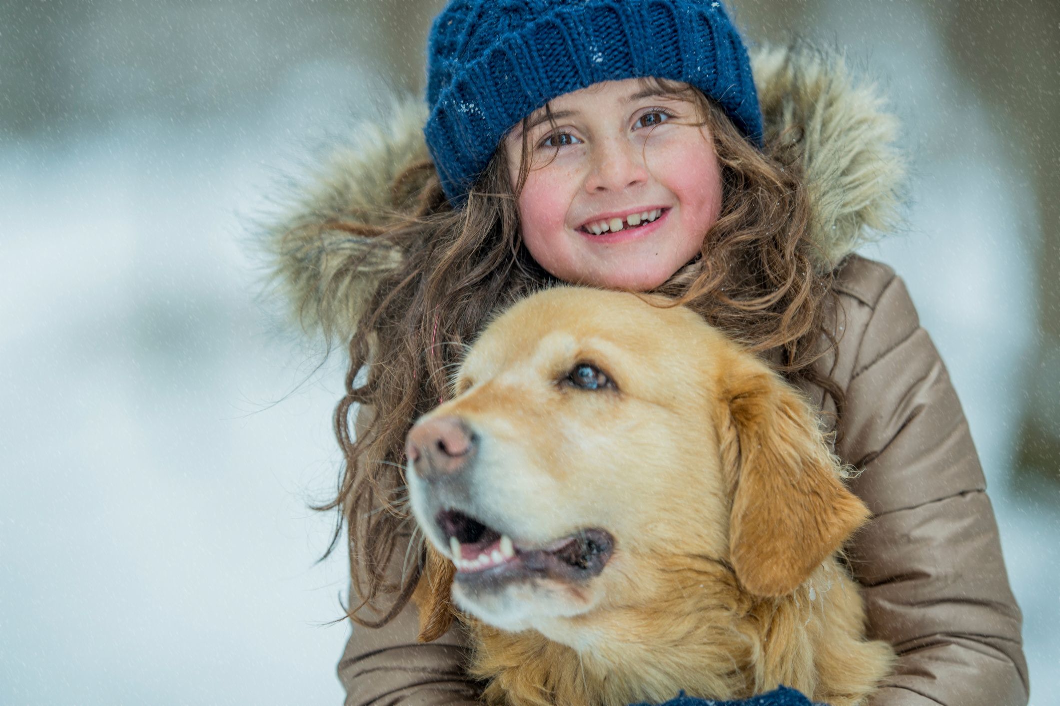 A smiling girl hugging her golden retriever.