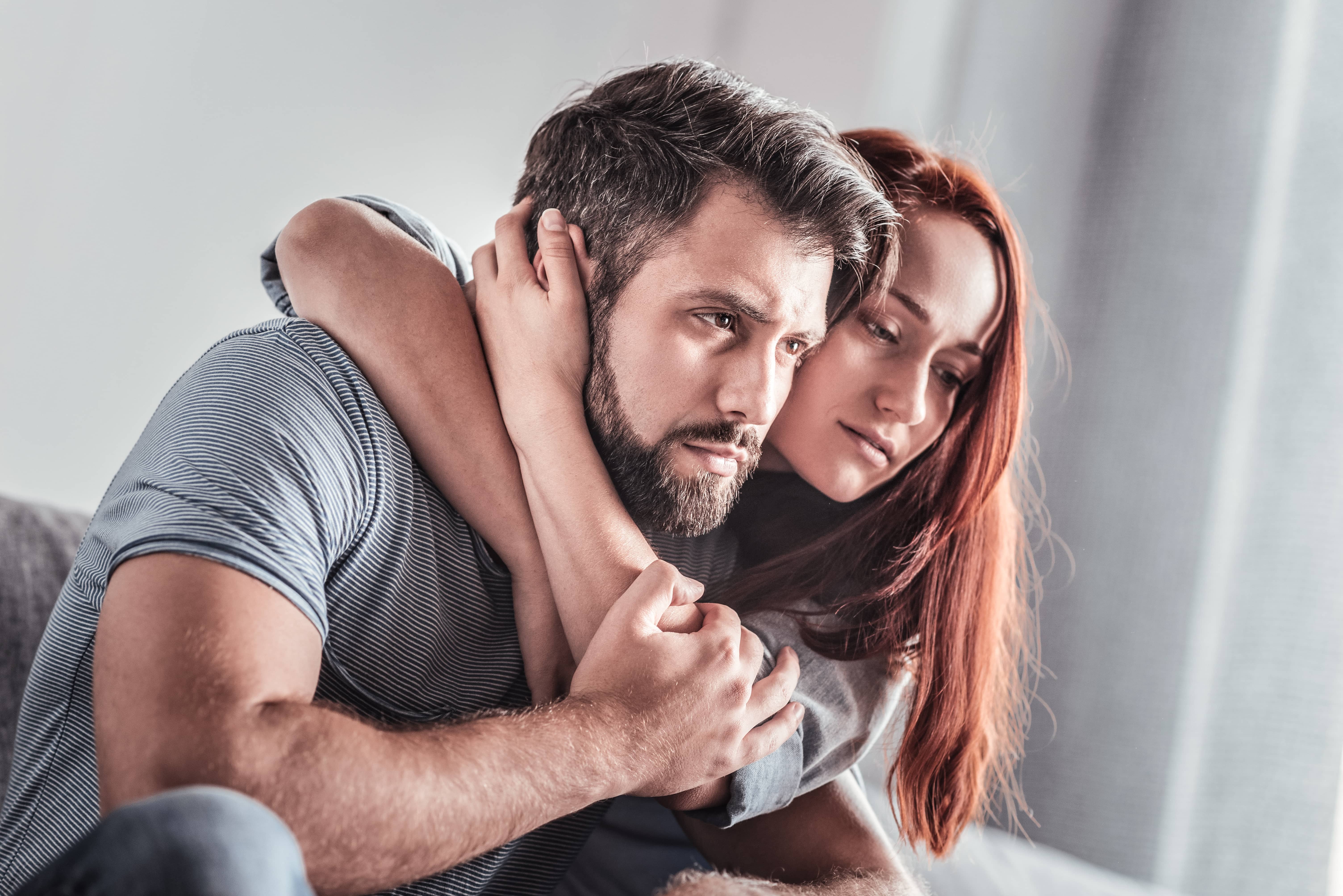 A woman holding a grieving upset man in her arms.