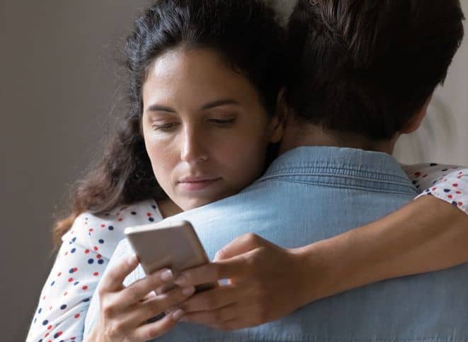 Woman hugging husband but on her phone_iStock-1277612588-modified-Compressed