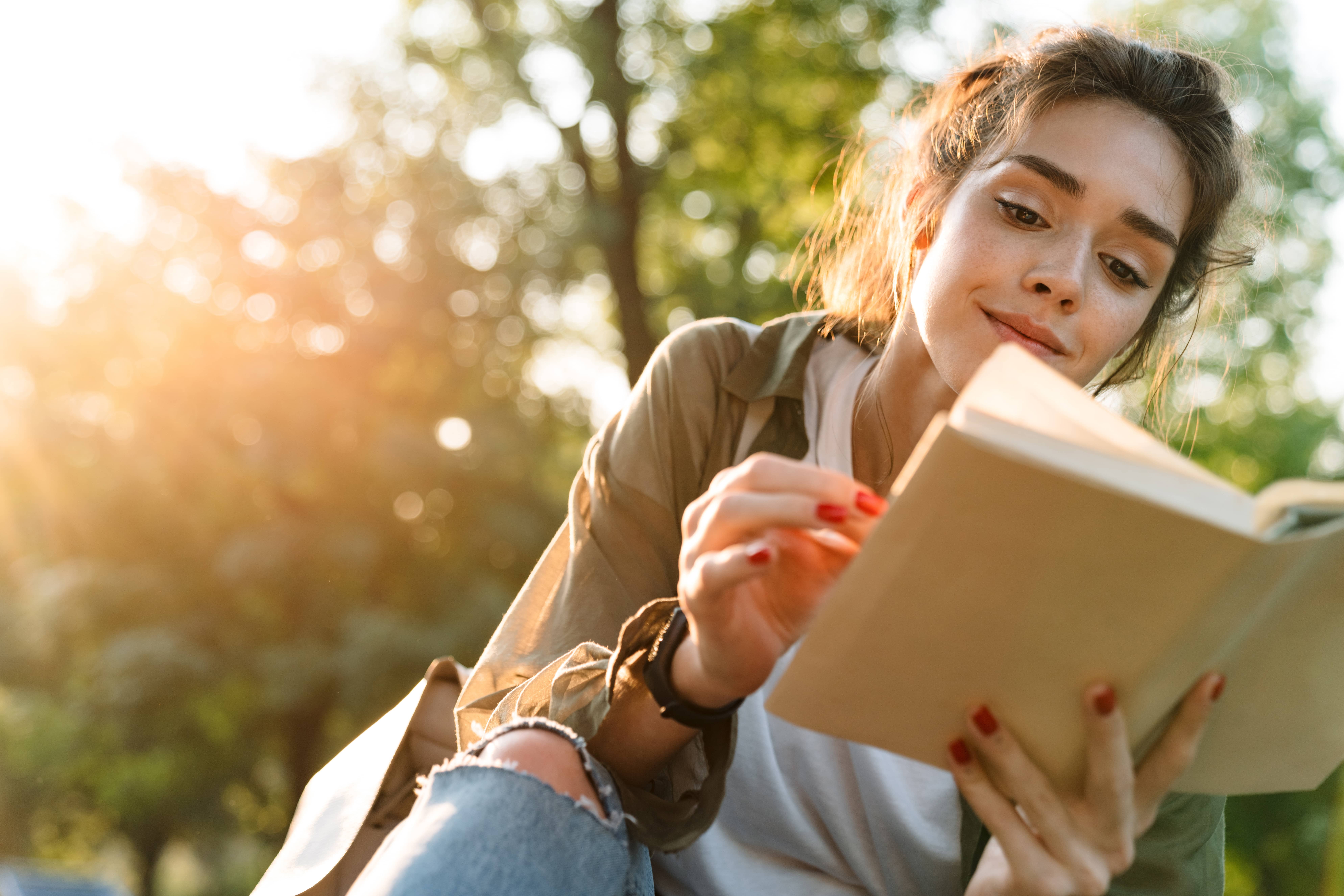 Woman changing a habit by choosing to read a book in park rather than surf social media on her smartphone..