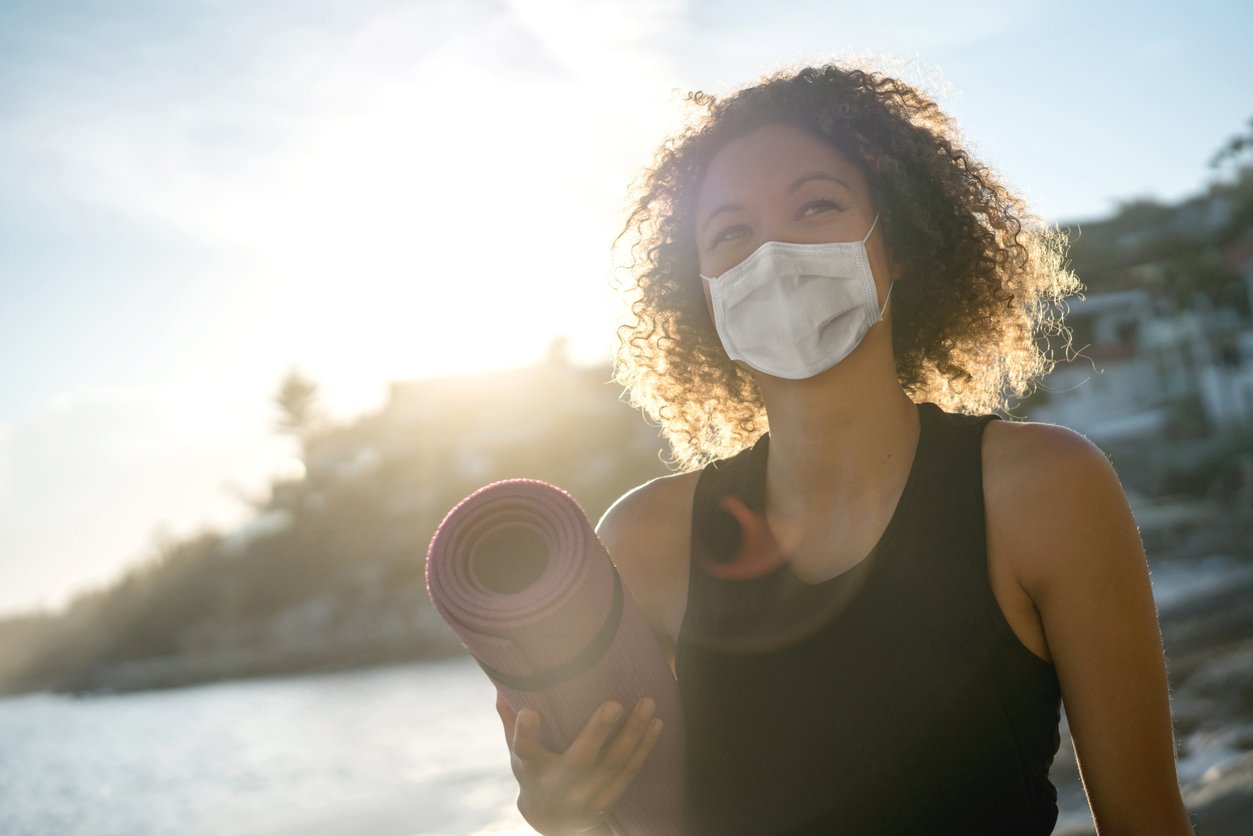 Woman wearing a COVID mask and holding a yoga mat