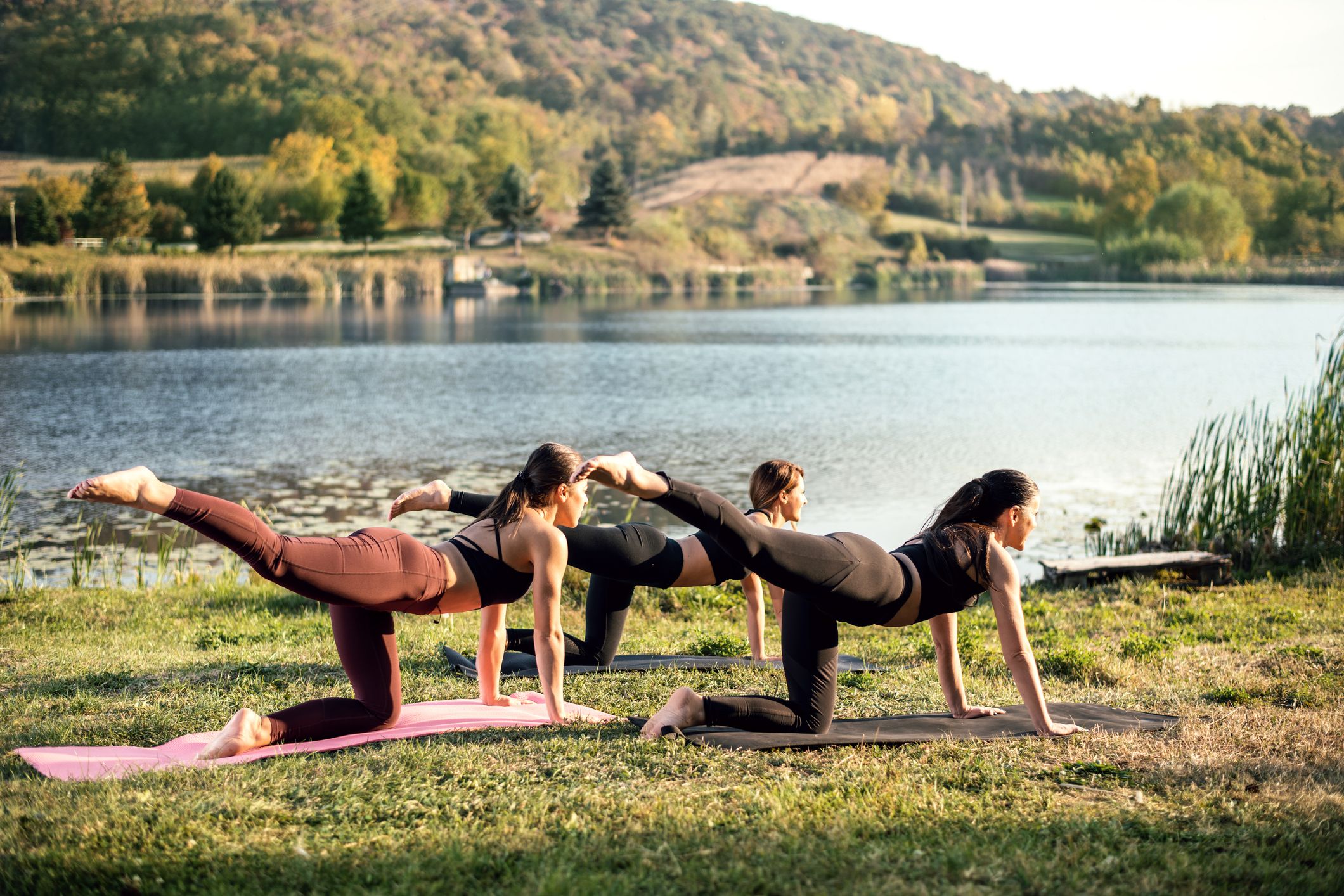 A self-care practice: women doing yoga outside by a lake.