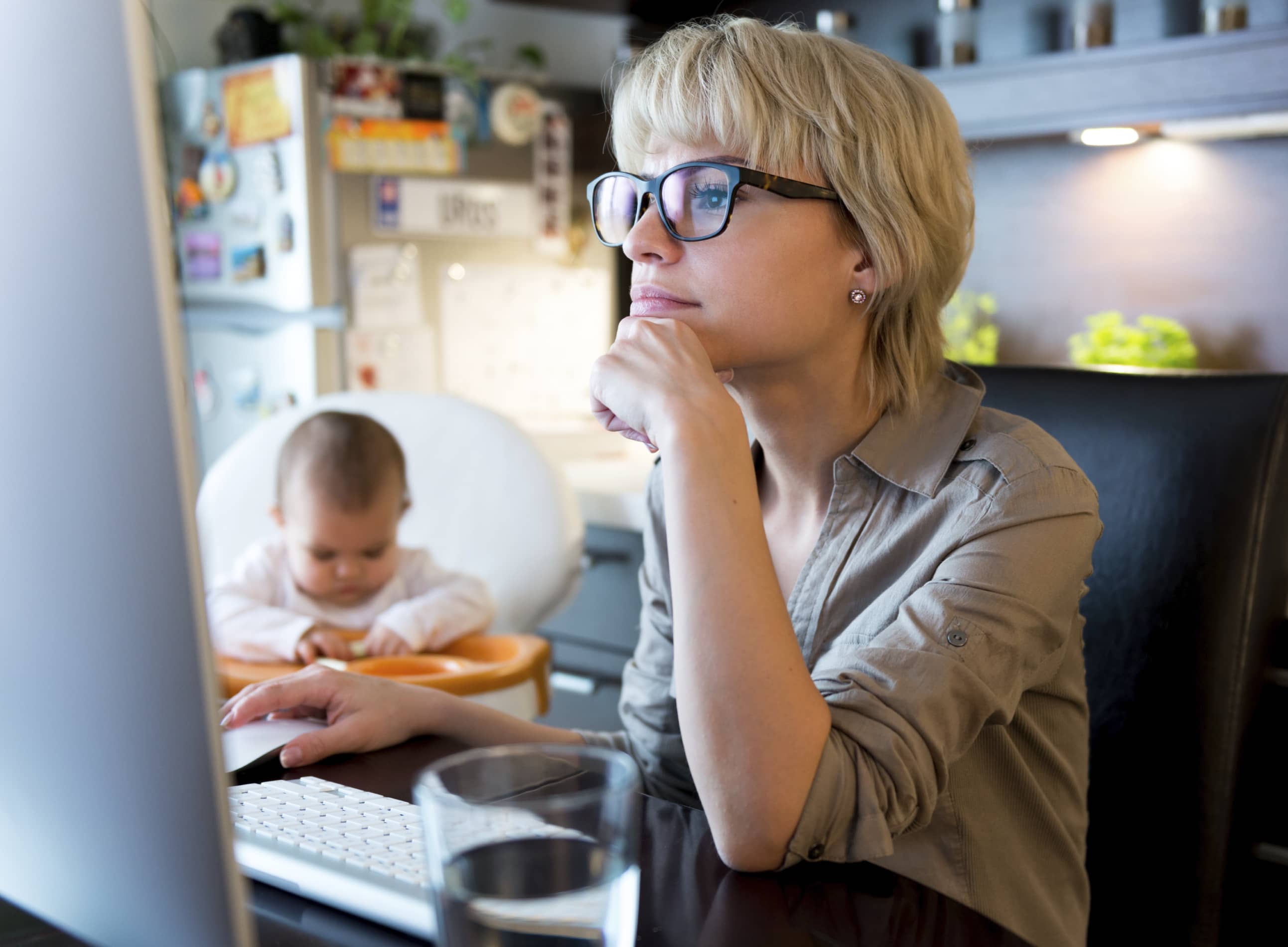 Mompreneur working at her computer with a baby looking on.