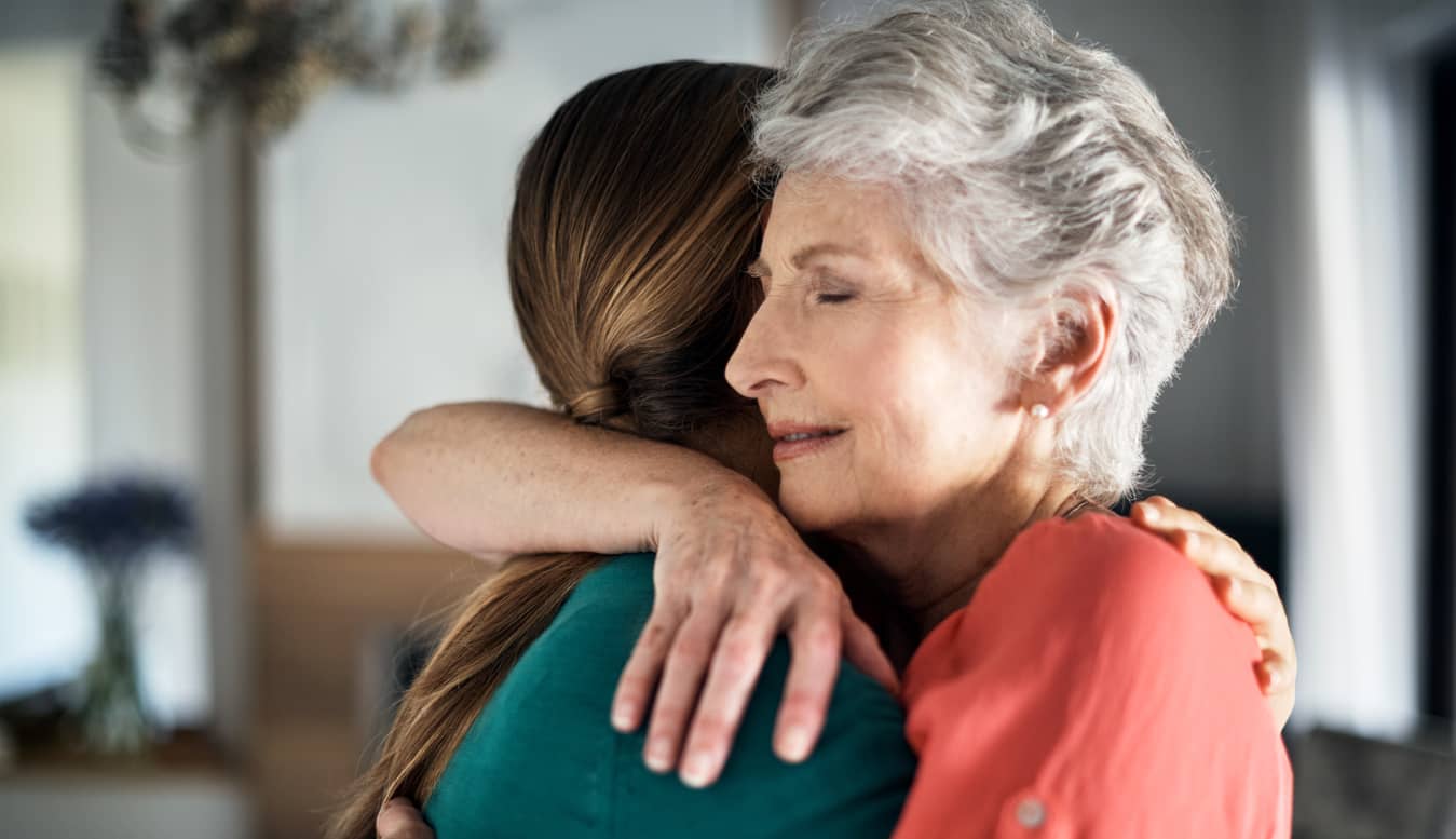 Grey-haired mother with eyes closed embracing her adult daughter with empathy.