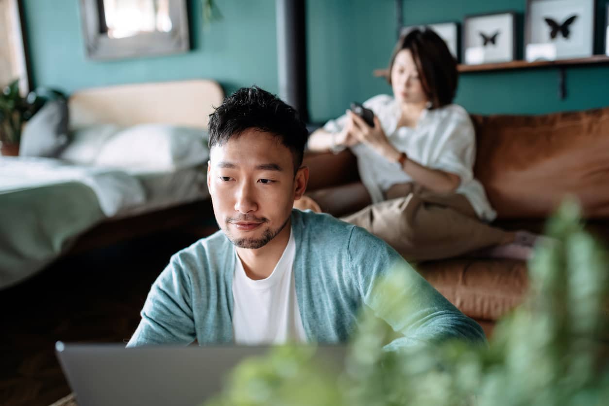 A young Asian couple on devices and sitting separately.