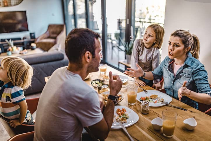 Young parents arguing at the dinner table in front of their children.