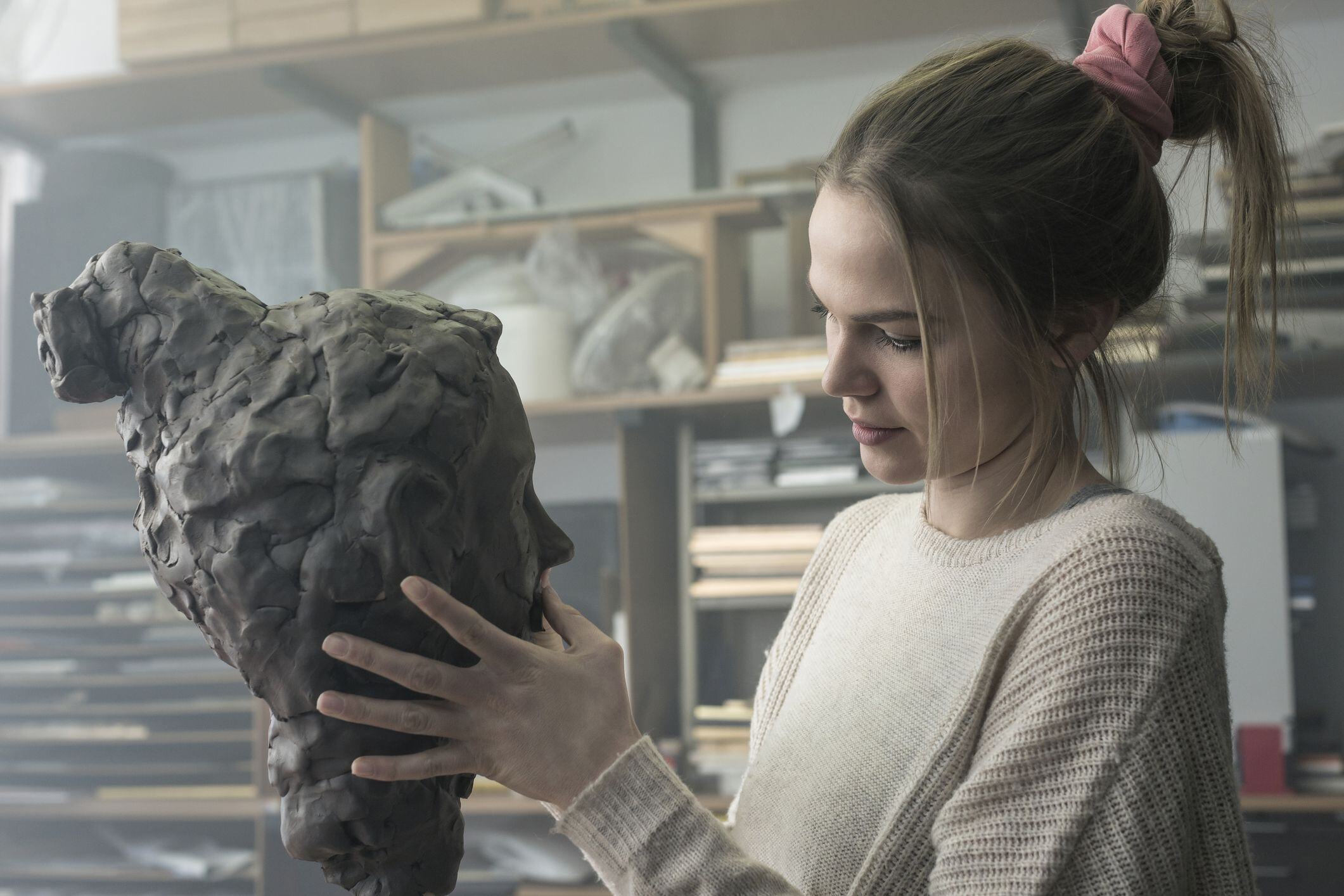A young woman creatively sculpting a bust with her hands.