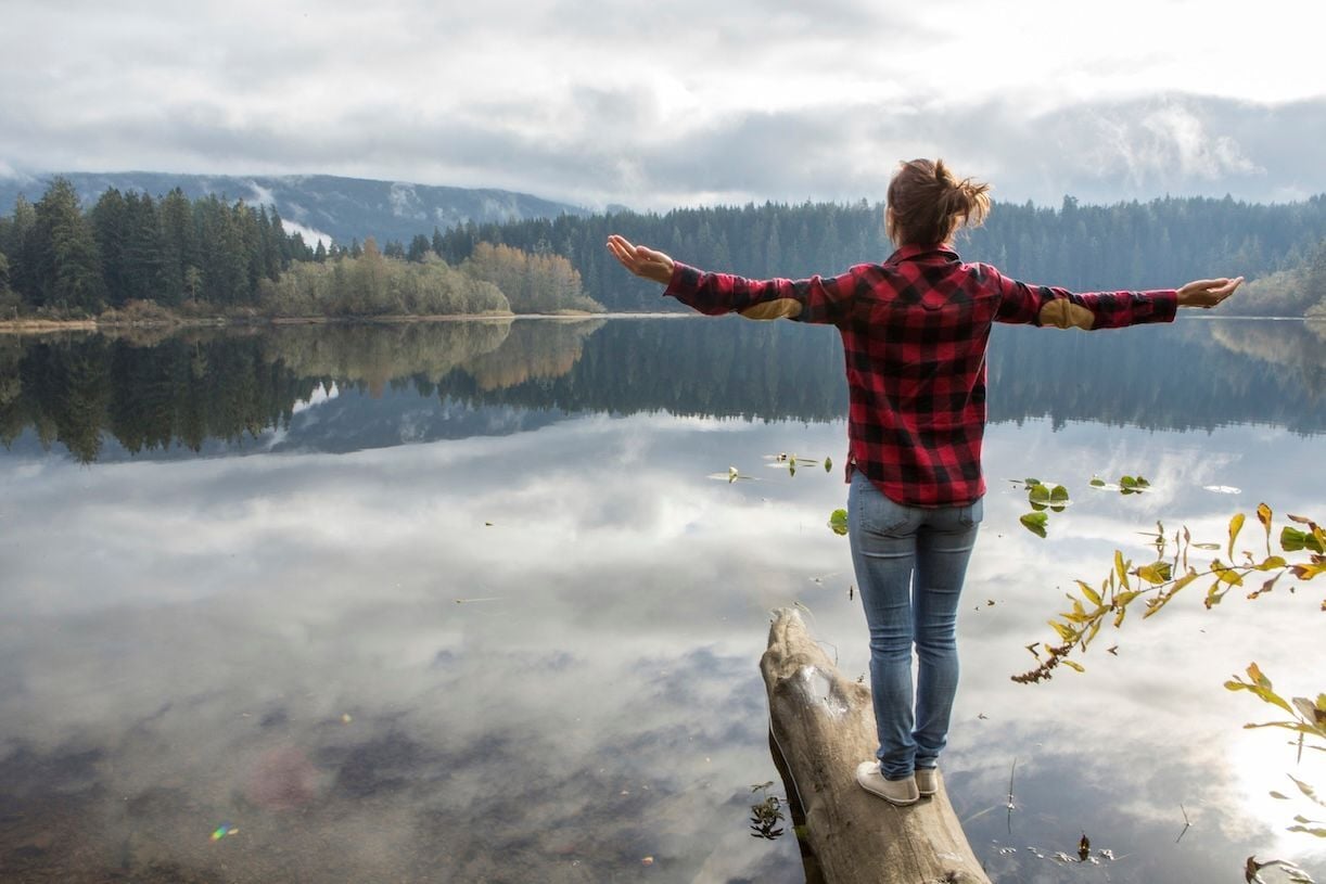 Young woman with self-love balancing on a tree log on a lake.