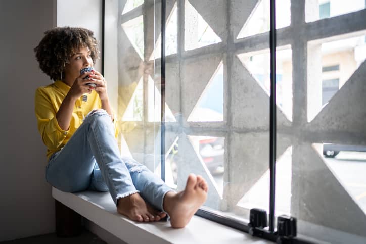 A woman sitting on a windowsill drinking herbal tea to relax before bed.