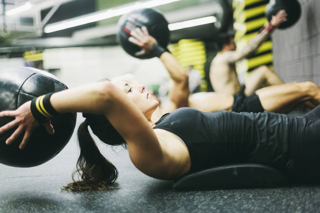 A young woman in a high intensity fitness workout with weighted balls at the gym.