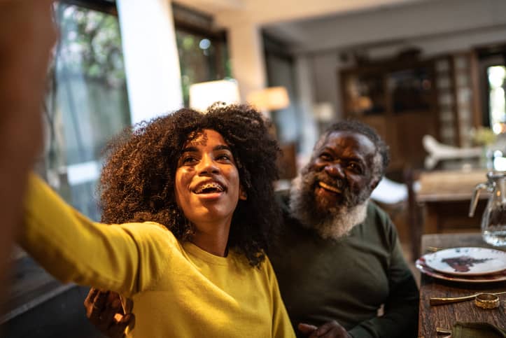 A young black woman taking a selfie with her father when visiting.