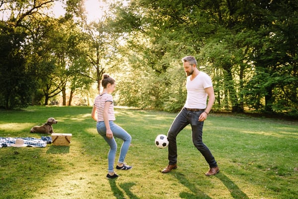 Father and teenage daughter playing soccer in a park.