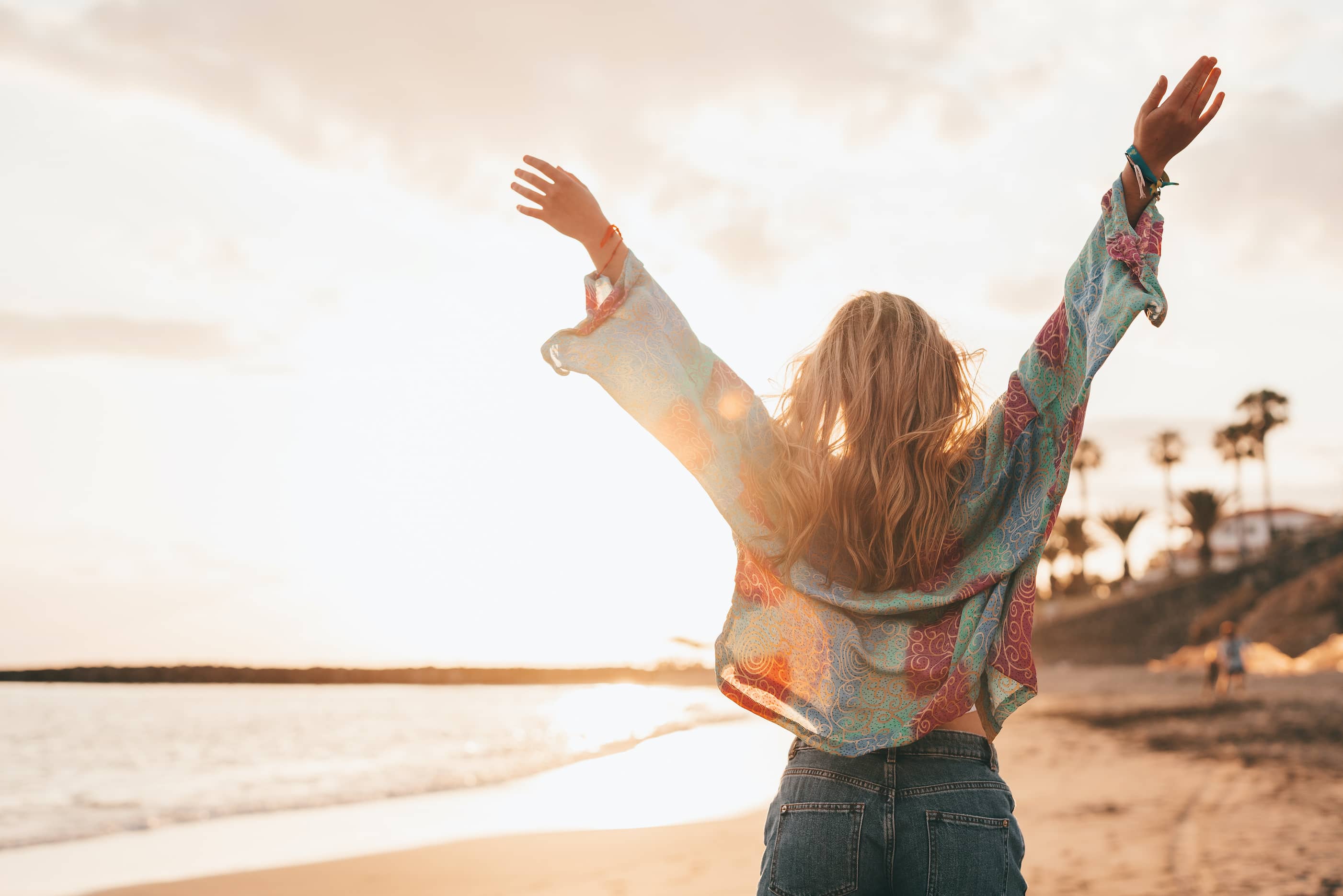 A joyful woman with arms in the air and walking on the beach.