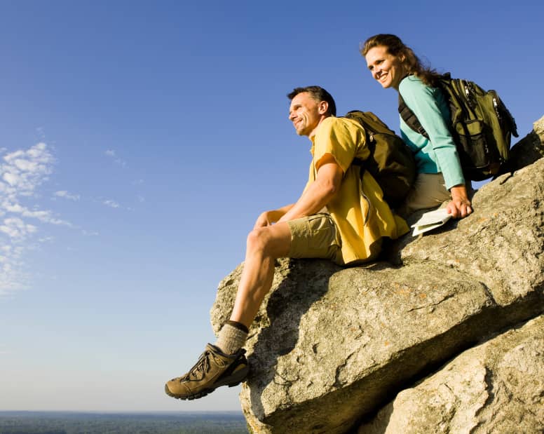 A couple sitting on a large boulder overlooking the horizon.